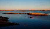 A red kayak is paddeling next to an island at dusk. 