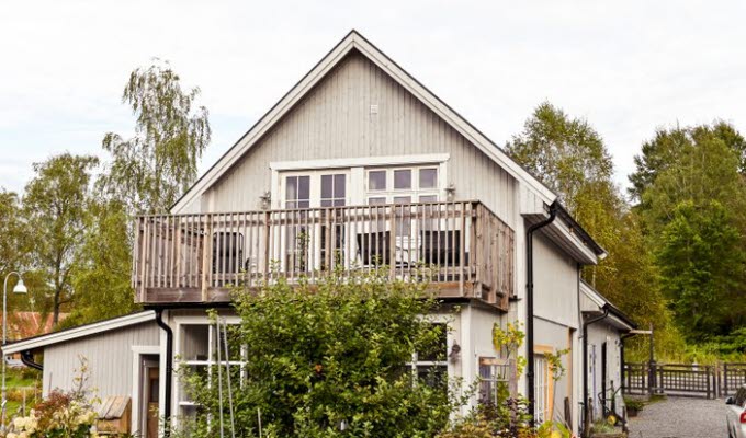 En bild på ett gråmålat hus med mycket buskar och grönska runtomkring