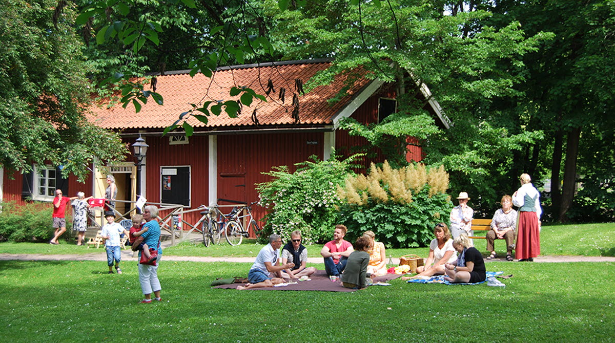 People sitting on the grass and have coffee and people who go on Turbinhusön, which is a park with beautiful old houses in Tidaholm.