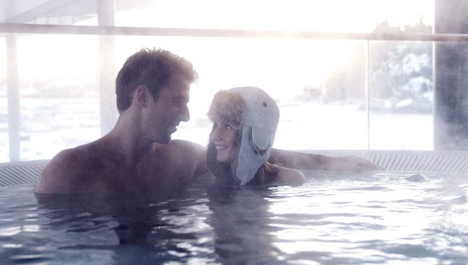 En kvinna och en man sitter tillsammans i jacuzzin på Strömstad Spa. Kvinnan har på sig en stor, vit mössa.