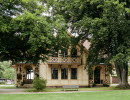 Light yellow wooden villa in park. Lots of big trees all around. 