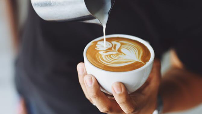 En person häller upp skummad mjölk i en kopp latte och formar mönstret av en tulpan