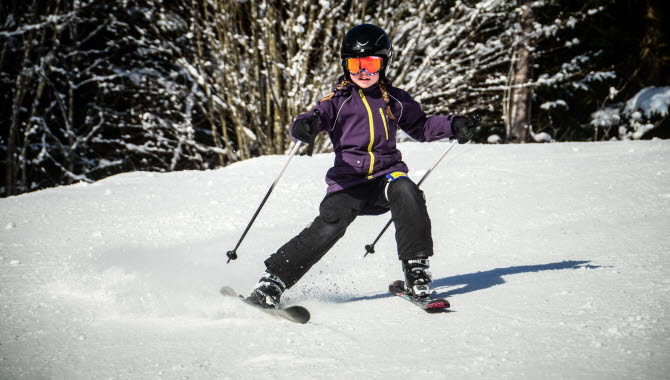 Girl goes downhill skiing, she has a black helmet and ski goggles.