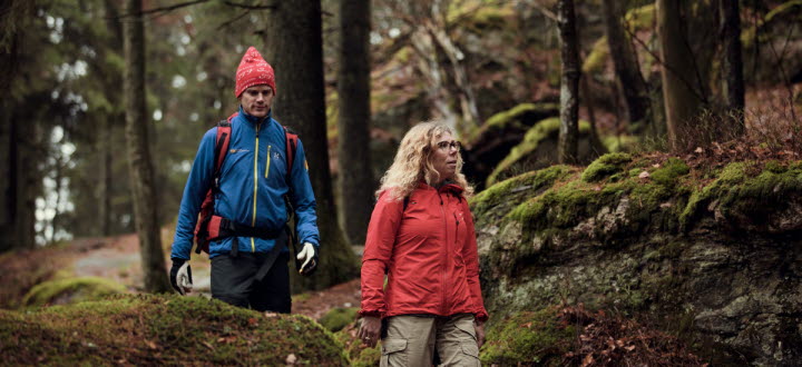 Två vandrare i färgglada kläder går genom en vacker skog
