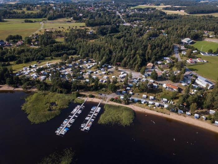 En flygbild över en campingplats intill en stor sjö. Här är båtar, husbilar och husvagnar uppställda på rad.