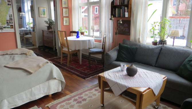 Interiör bild på ett rum med soffa, soffbord och en dubbelsäng. Parkettgolv med stora gamla fönster. Öppning in till ett annat rum. 