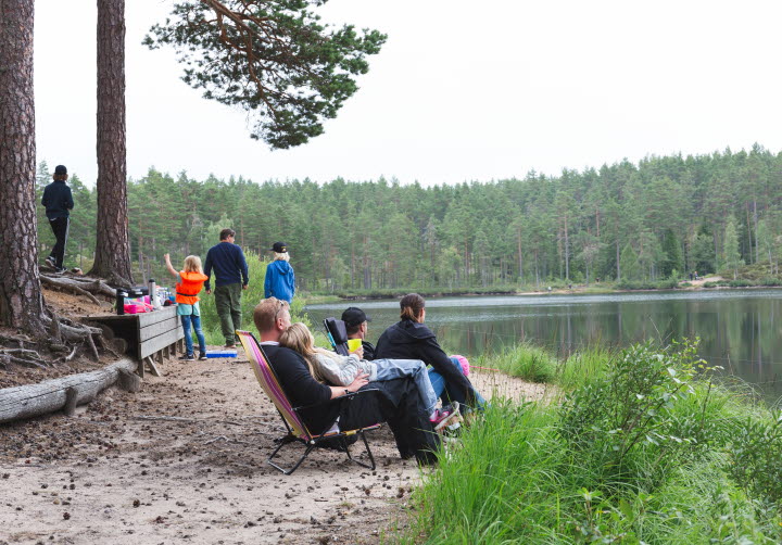 Personer som sitter och står intill en fiskesjö på Hökensås naturområde utanför Tidaholm.