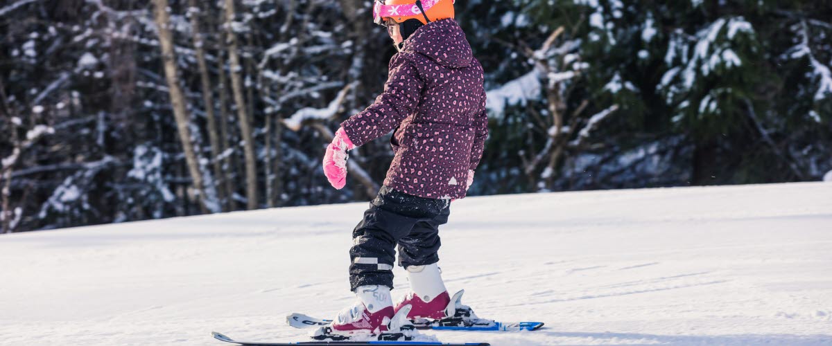 En flicka i overall och rosa hjälm åker skidor i backen.