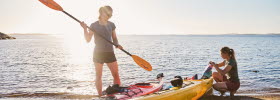 Two women on the beach by their kayaks.