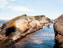 En person i kajak paddlar igenom en smal kanal mellan två klippor i Kosterhavet utanför Kosteröarna.