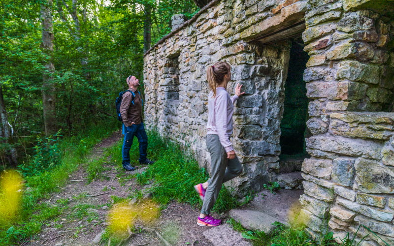 Two people, a man and a woman, view a stone cave in the forest.
