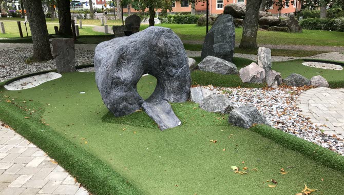 Minigolfbana med grönt konstgräs. En rund sten som man skjuter bollen igenom.