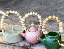 Three teapots in different colors of ceramics. They have wooden handles made of beads