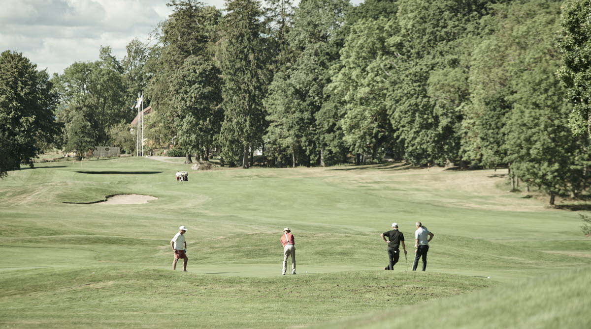 Golfbana med fyra personer som spelar golf, personerna är ganska långt bort i bilden.
