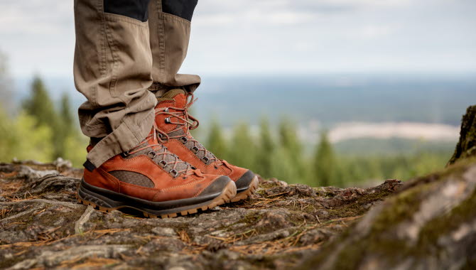 Ben i röda skor ståendes på en klippa med utsikt över skog och vidder