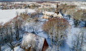 Ett drönarfoto av en stor stenkyrka och en träbyggnad. På marken ligger ett tunt lager snö.