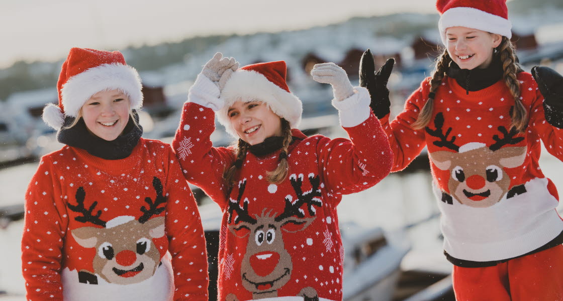 Tre julklädda flickor med tomteluva och sticktröja med renmotiv