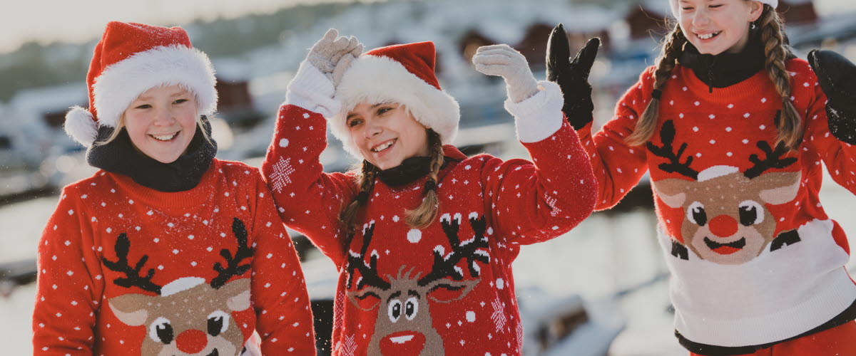 Tre julklädda flickor med tomteluva och sticktröja med renmotiv