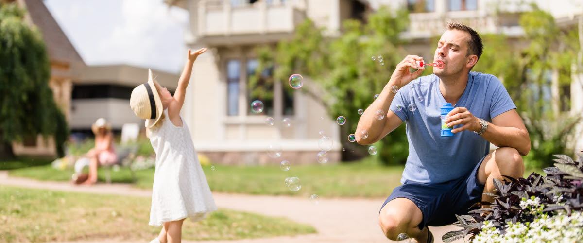 Far och dotter blåser såpbubblor i Hjo Stadspark. 