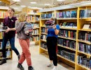 Tre personer i biblioteket som bär på böcker. 