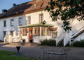 En bild på ett stort vitt hus av trä med röda och gröna detaljer runt fönstren.