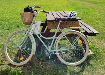 En grön cykel står lutad mot ett picknickbord. På bordet sitter en skylt med texten "Rastplats nybygget".