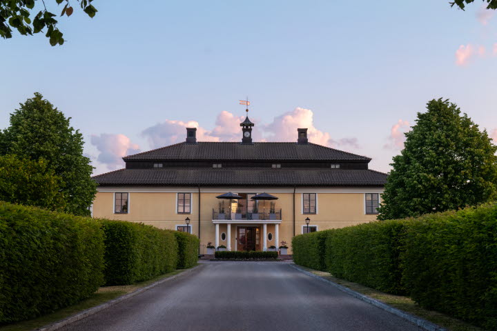Ett gult stort hus med häck framför