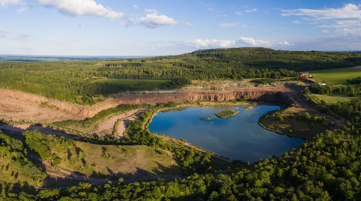 Flygbild över Stora Stenbrottet på Kinnekulle. Sjö i mitten omgiven av berg och skog.