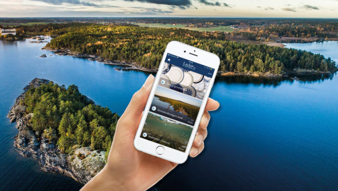 En hand som håller i en mobil framför en vy med skärgård