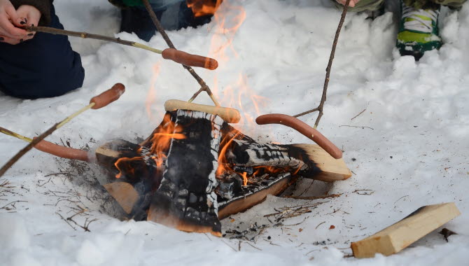 Korvgrillning i snö över öppen brasa.