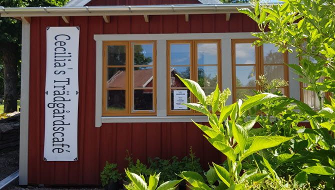 Rött hus med vita knutar omgivet av en grön blommande trädgård.