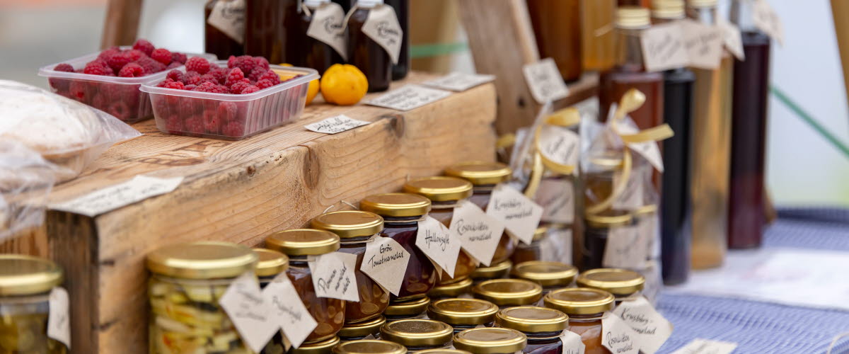 Varierade lokalproducerade produkter på ett marknadsstånd så som marmelad och bär.