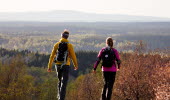 Två personer i färgglada kläder vandrar bort från kameran med en vindunderlig utsikt över Vallebygden. 