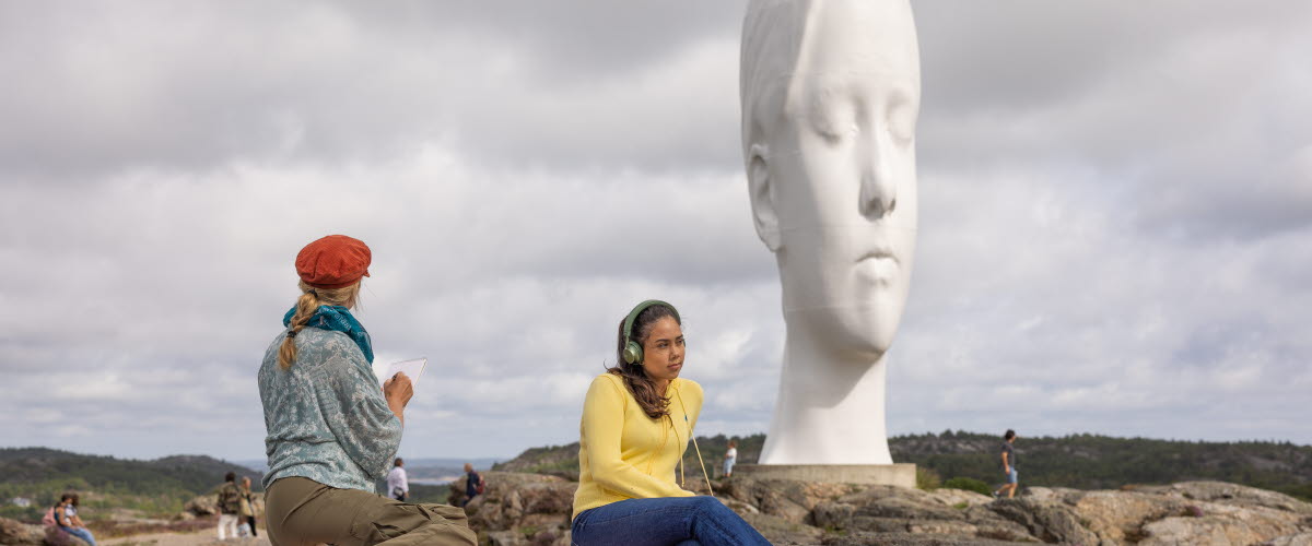 Två kvinnor sitter på en klippa i en skulpturpark.