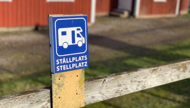 Ställplatsskylt i närbild med Café Åsle i bakgrunden.