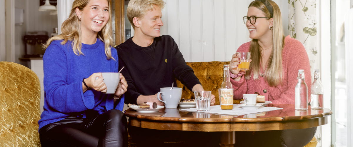 Två kvinnor och en man sitter och fikar på ett café. 