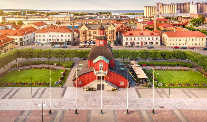 Rådhuset- en röd träbyggnad med fyra våningar. Bilden är tagen något uppifrån vilket gör att det går att skymta sjön Vänern i bakgrunden. i bakgrunden syns även flertal hus och byggnader. 