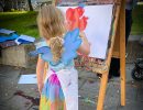 Child with long hair in a braid paints with watercolors on easel.

