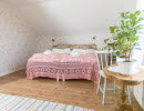 A double bed with pink crochet bedspread, wooden floor and a tiled stove.