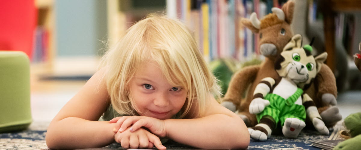 Liten flicka ligger på golvet och läser en bok