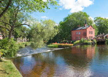 Vy över Kaffestugan och Turbinhuset (konsthall) på Turbinhusön i Tidaholm, med ån Tidan framför.