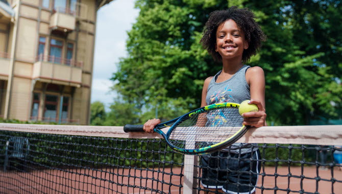 Tjej spelar tennis utomhus i Hjo Stadspark.