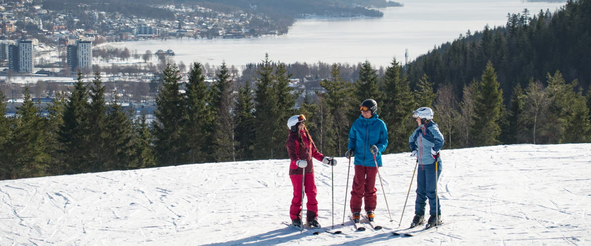 Three children in colorful clothes with skis on top of Ulricehamn Ski Center.