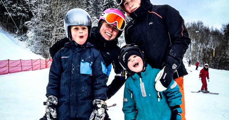 Mamma med tre barn ler mot kameran. Alla har skidutrustning på sig. 