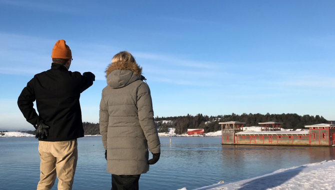 En man och en kvinna står och blickar ut över havet och Strömstads kallbadhus i vinterskrud.