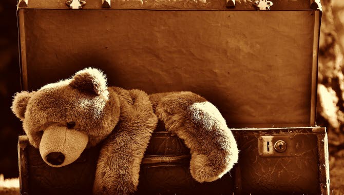 En teddybjörn ligger halvvägs nerstoppad i en gammaldags resväska. Hela bilden är sepia-tonad i brunt.