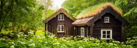 Old cottages in brown with grass on the roof. Lush and green nature all around.