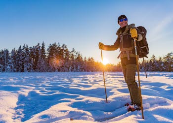 A beautiful sunny winter landscape. A person stands in the snow with skis on his feet and ski poles in their hands.
