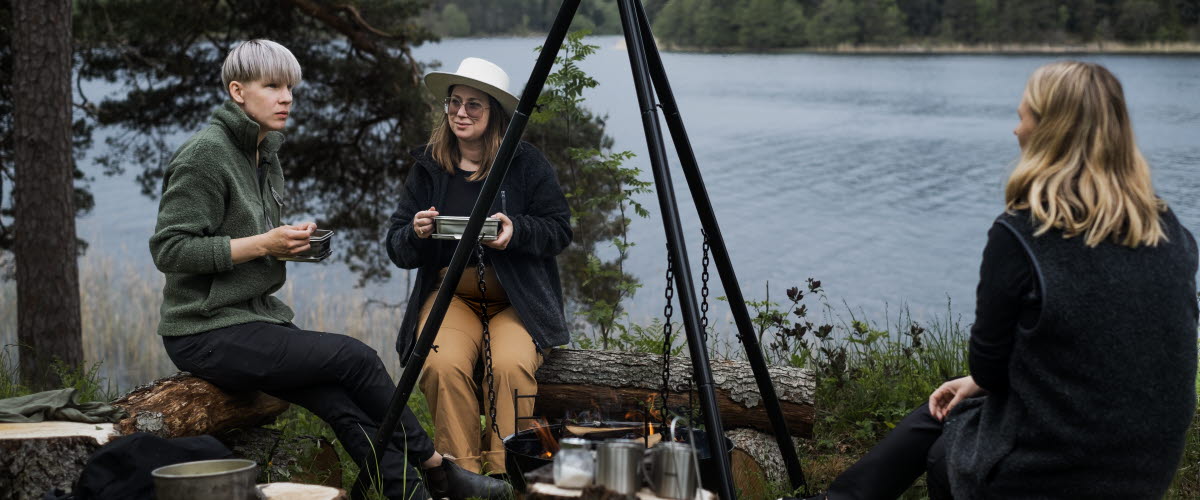 Vänner sitter runt eld och njuter av en måltid i Dalsland