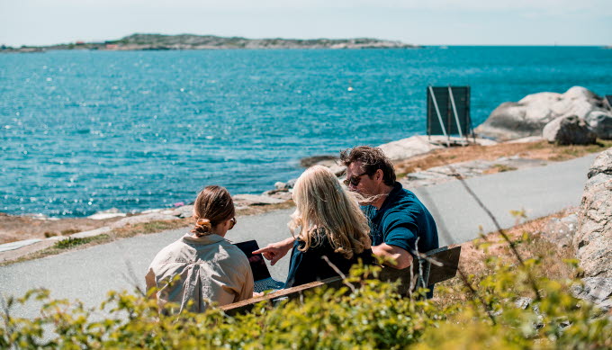 Människor sitter på en bänk vid havet.